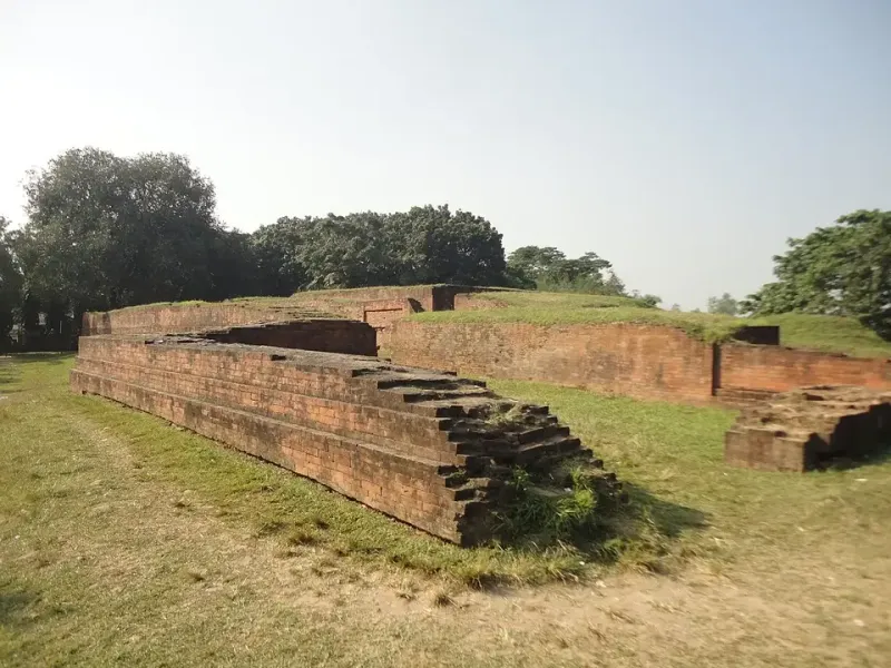 মহাস্থানগড়ের পুরোনো ইটের প্রাচীর ও ধাপে ধাপে ভাঙা ইটের স্তূপ, চারপাশে ঘাস ও গাছ