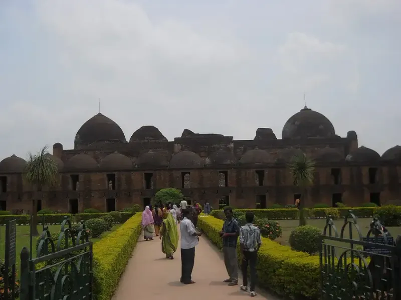 মুর্শিদাবাদের কাটরা মসজিদ: সামনে বাগানের পথ, পেছনে লাল ইটের লম্বা দোতলা সারিঘরের ওপর অনেক ছোট গম্বুজ