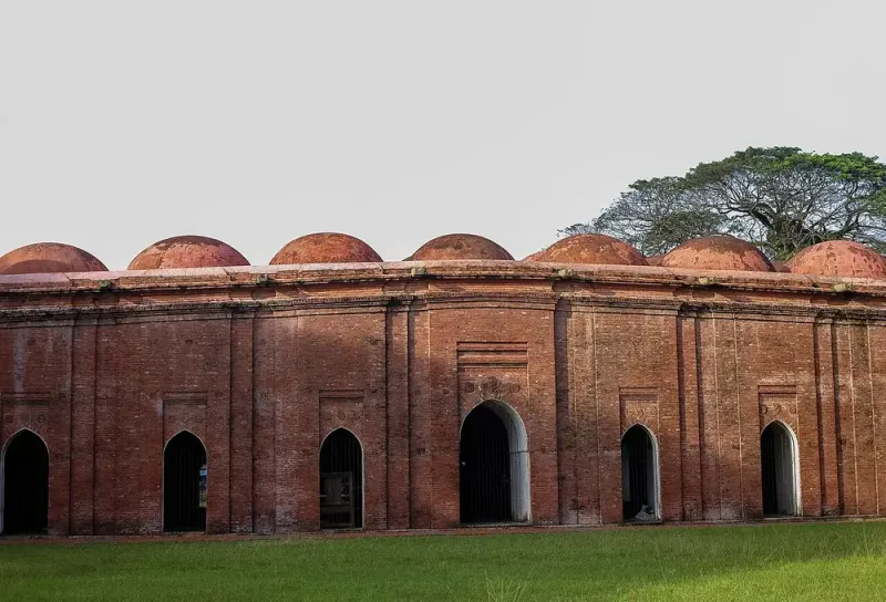 লাল ইটের লম্বা মসজিদ, ছাদজুড়ে সারি সারি গোলাকার গম্বুজ, দেয়ালে খিলানযুক্ত দরজা