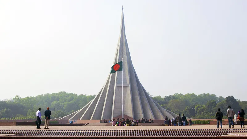 সাভারে ত্রিভুজাকার দেয়ালের সারি নিয়ে উঁচু জাতীয় স্মৃতিসৌধ, সামনে জাতীয় পতাকা