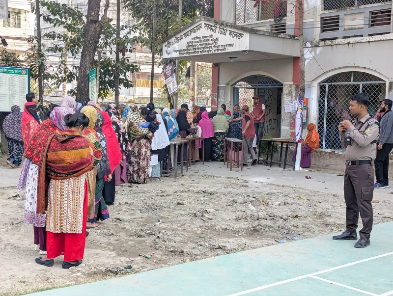 ভোটকেন্দ্রের সামনে লাইনে দাঁড়ানো নারী ভোটার, পাশে একজন নিরাপত্তাকর্মী